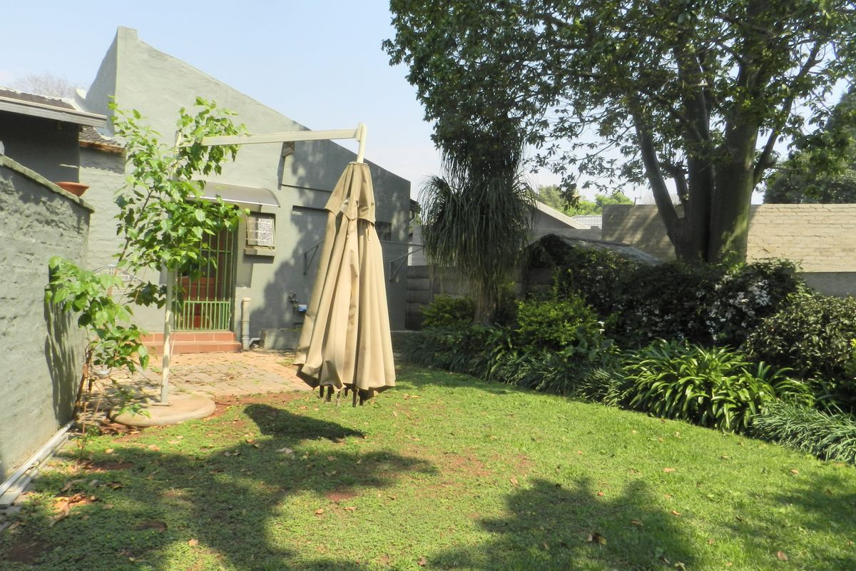 A private rear garden featuring a paved patio area, established trees, and a secure entrance to the main dwelling.