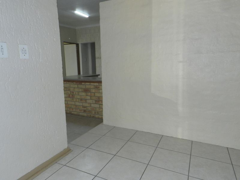 An open plan living area featuring tiled flooring and a brick breakfast bar, leading into a kitchen space.