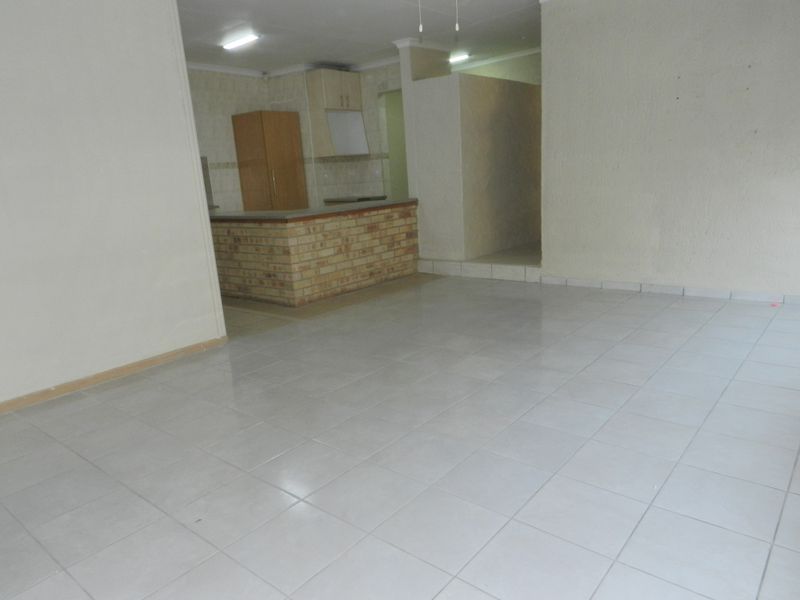 An open-plan living and kitchen area featuring tiled flooring, a brick breakfast bar, and built-in cabinetry in a neutral, vacant space.