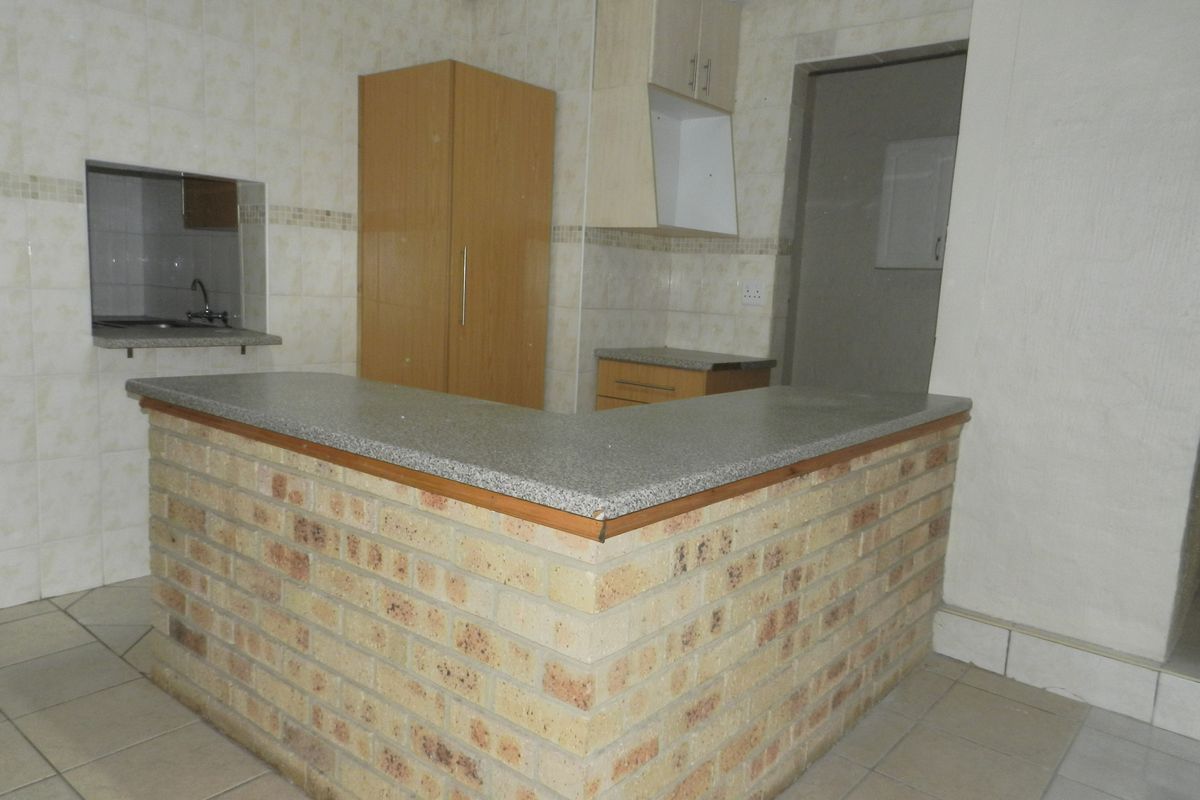 A dated kitchen featuring a brick breakfast bar, granite countertops, and tiled finishes, offering a functional layout ready for modern renovation.