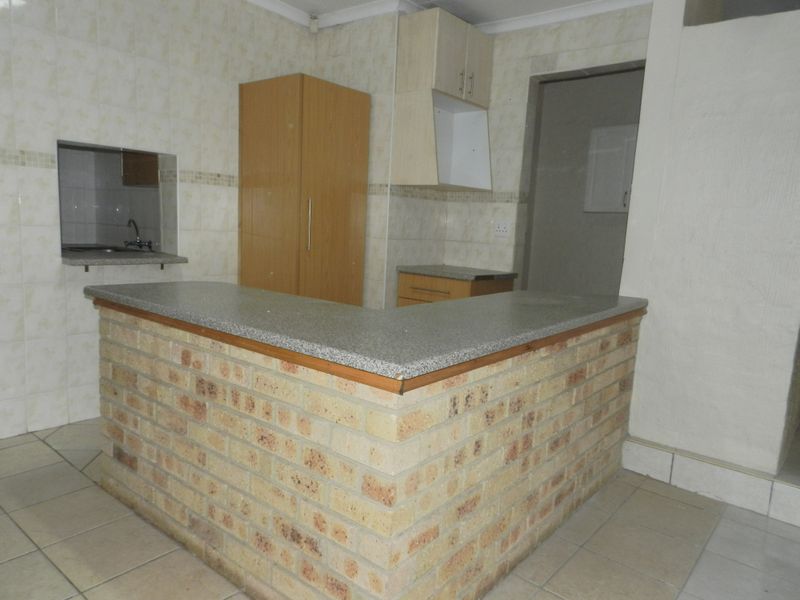 A dated kitchen featuring a brick breakfast bar, granite countertops, and tiled finishes, offering a functional layout ready for modern renovation.