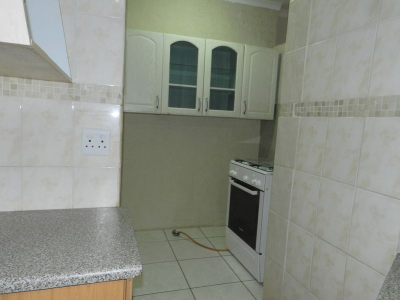 A functional kitchen area featuring built-in cabinetry, tiled splashbacks, and a freestanding gas stove with tiled flooring.
