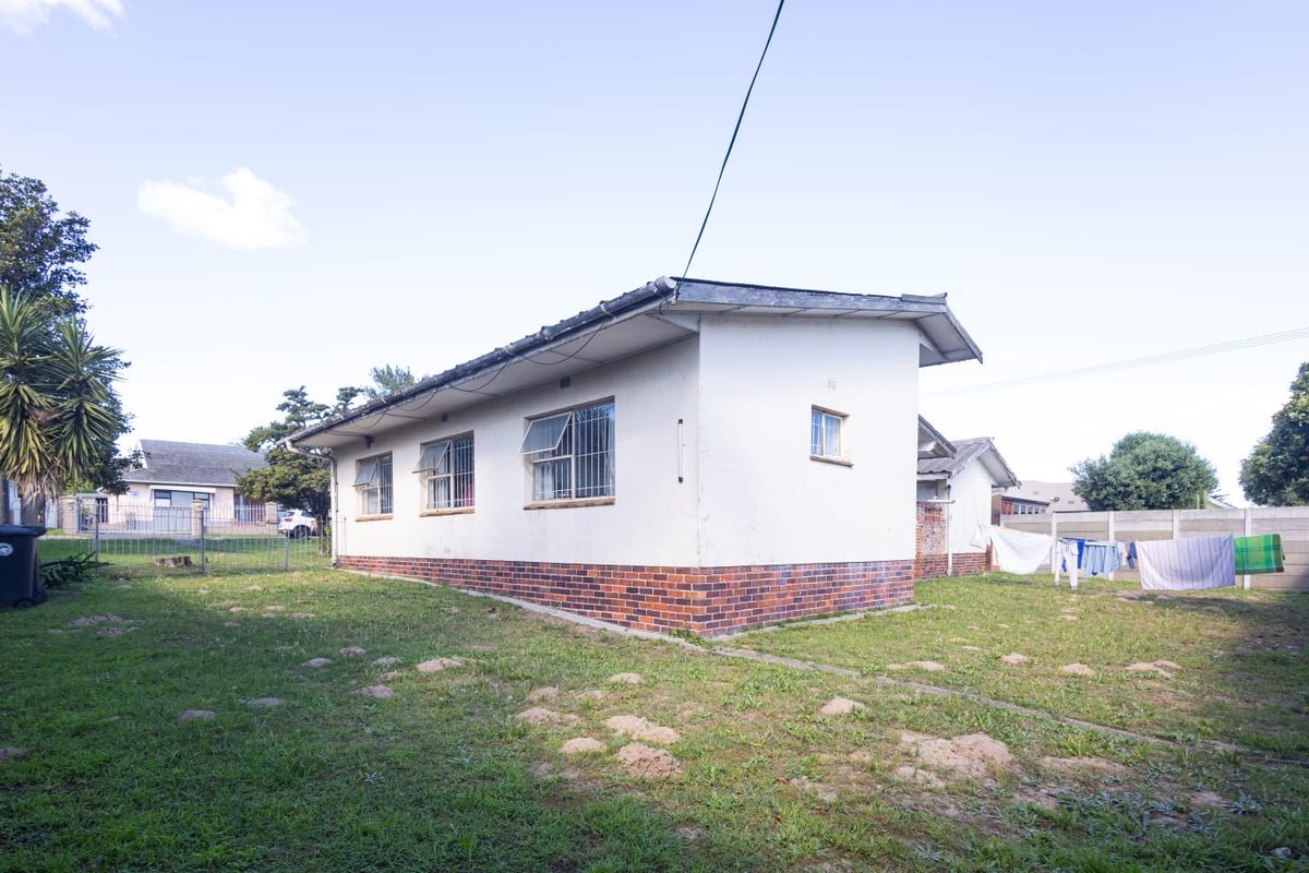 Rear view of the property showing the exterior brick and plaster facade, security-fitted windows, and a spacious backyard with boundary walling.