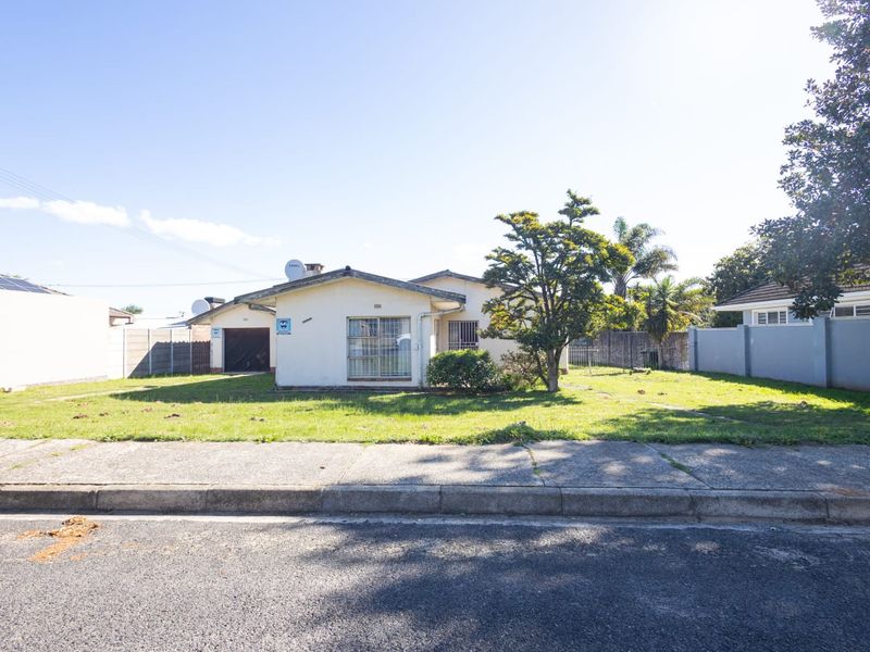 Front view of a single-story residential house featuring a large front lawn, concrete driveway, and secure perimeter walling.