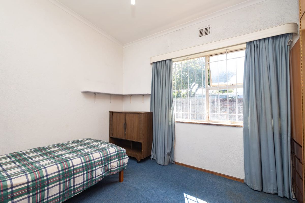 A bedroom featuring blue carpeting, security bars on the window, and built-in wall shelving, offering a functional space ready for modernization.