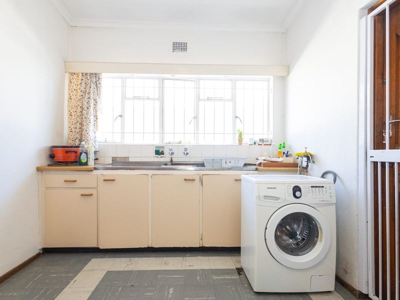Functional laundry area featuring built-in cabinetry, a stainless steel sink, and tiled splashback, with security features on the window and door.