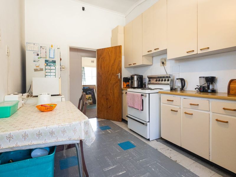 A functional kitchen featuring original cabinetry, a freestanding stove, and durable vinyl flooring, offering potential for a modern renovation.