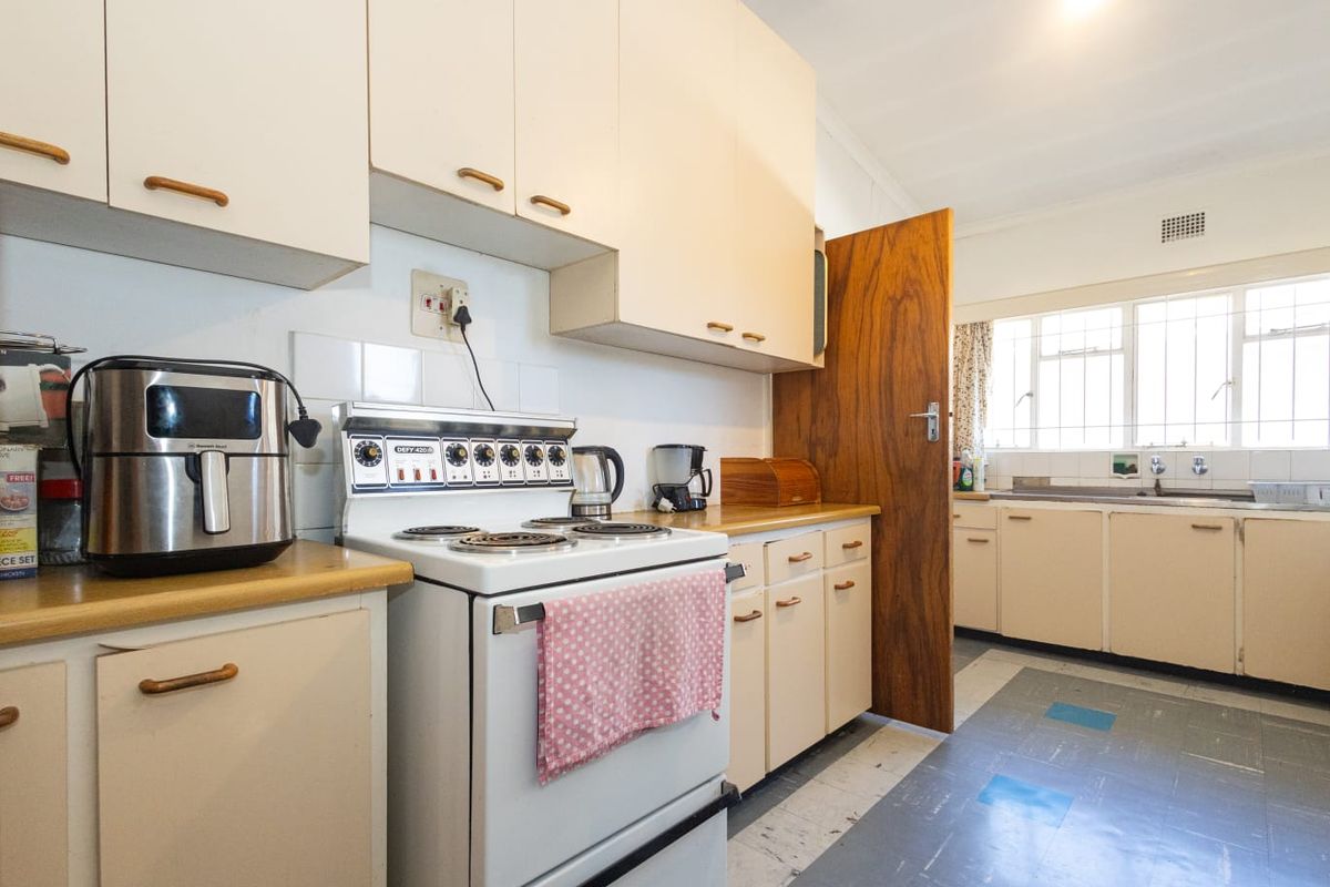 A functional kitchen featuring original cabinetry, laminate countertops, a freestanding electric stove, and a double basin sink with a window view.