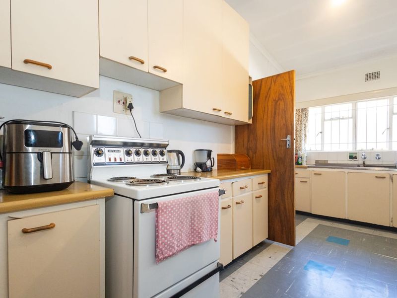 A functional kitchen featuring original cabinetry, laminate countertops, a freestanding electric stove, and a double basin sink with a window view.