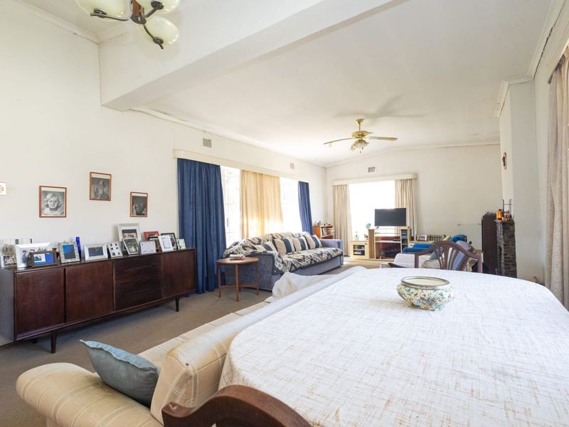 Spacious open-plan living and dining area featuring a fireplace, ceiling fan, and large windows with curtain rails.