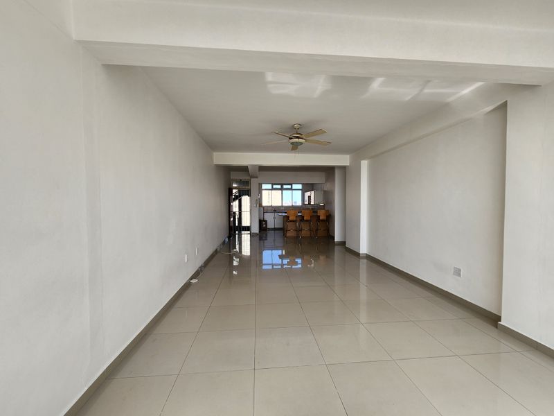 Spacious open-plan living and kitchen area featuring neutral tiled flooring, a ceiling fan, and built-in kitchen cabinetry.