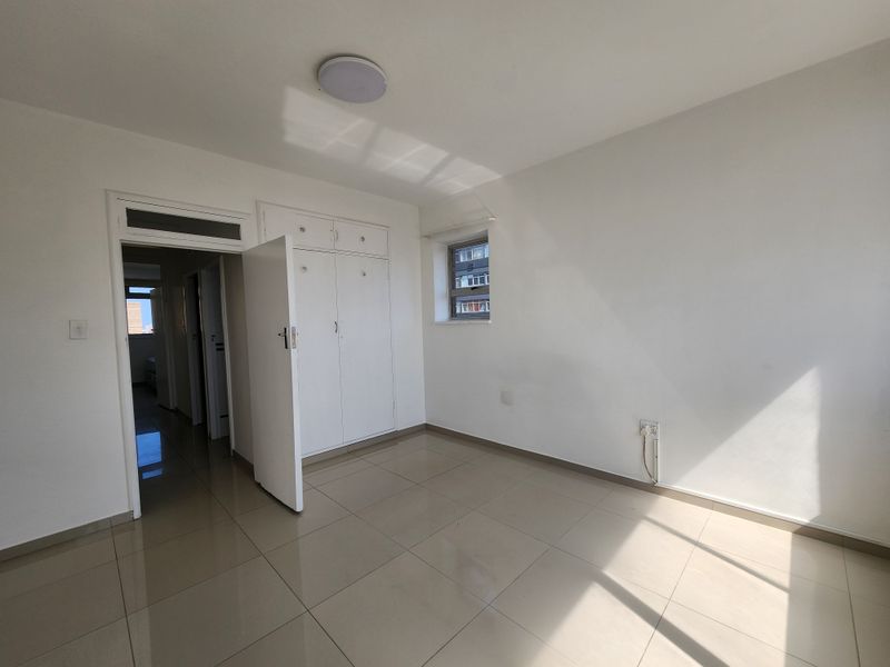A bright, empty bedroom featuring neutral tiled flooring, built-in storage cupboards, and a clean, minimalist aesthetic ready for personalization.