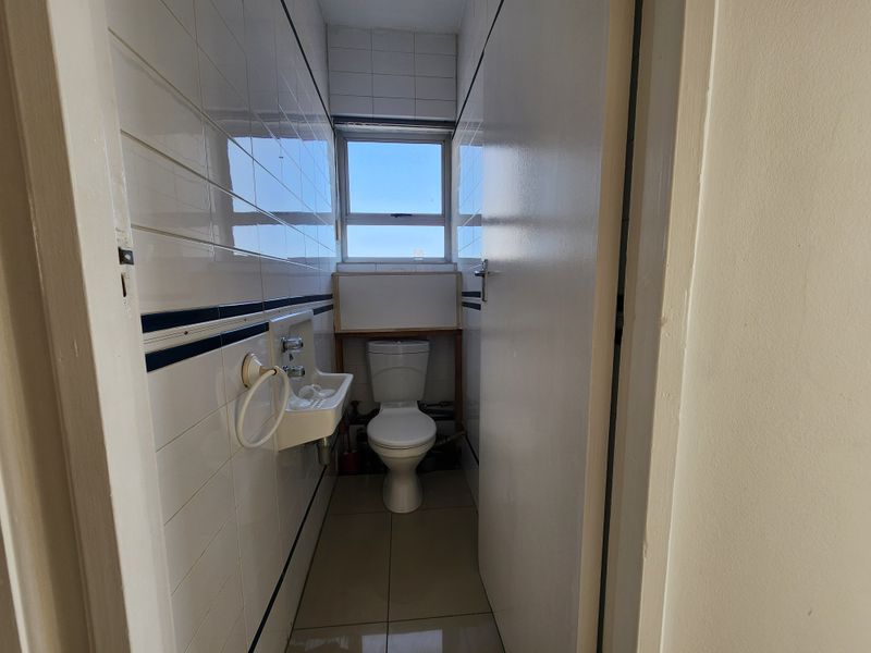 A compact, tiled bathroom featuring a wall-mounted basin and toilet, requiring cosmetic updates to improve its dated appearance.