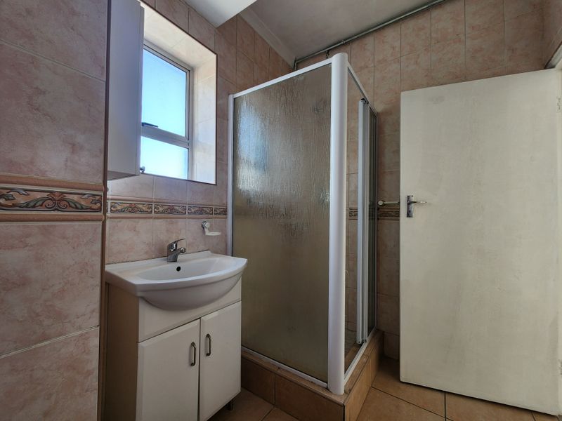 A functional bathroom featuring a shower enclosure, vanity basin, and tiled finishes, offering potential for modernization and aesthetic updates.