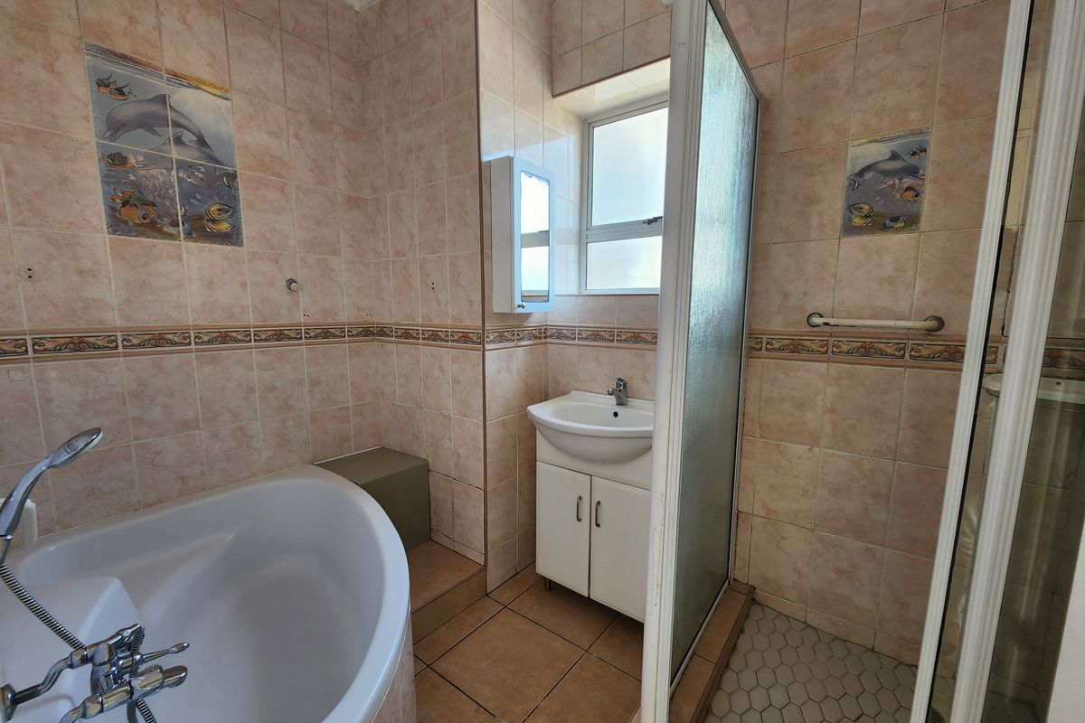 A functional bathroom featuring a corner bathtub, separate shower enclosure, and a vanity cabinet with tiled walls and flooring.