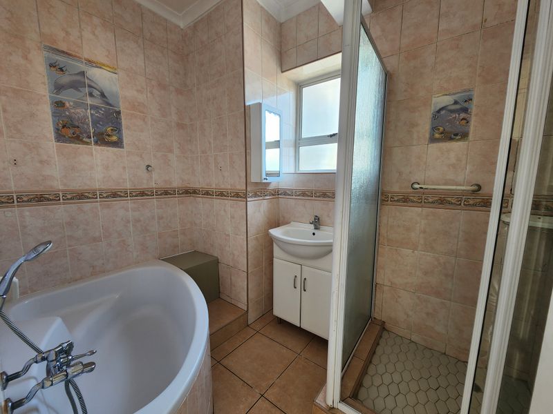 A functional bathroom featuring a corner bathtub, separate shower enclosure, and a vanity cabinet with tiled walls and flooring.