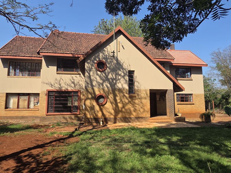A two-story residential house featuring a tiled roof, brick and plaster facade, and multiple casement windows, set within a spacious garden area.