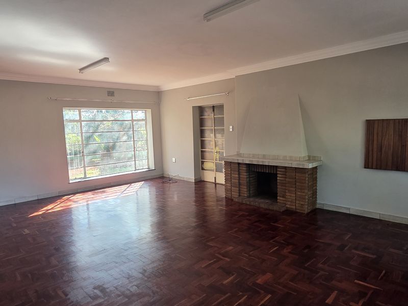 Spacious living room featuring classic parquet flooring, a traditional brick fireplace, and large steel-framed windows providing ample natural light.