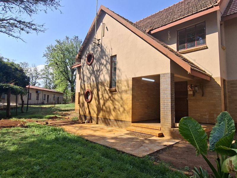 Rear view of the house featuring a brick and plaster facade, a covered patio area, and access to the surrounding garden space.