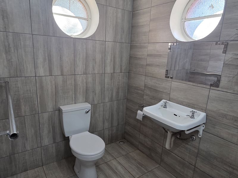 A clean, modern bathroom featuring grey wood-look porcelain tiling, a wall-mounted basin, and distinctive circular windows.