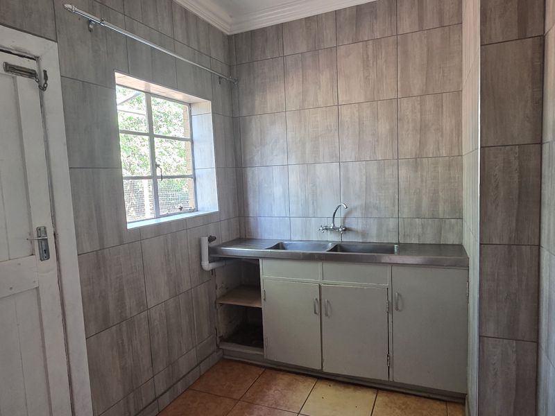 A functional laundry area featuring full-height wall tiling, a stainless steel sink, and built-in cabinetry with space for appliances.
