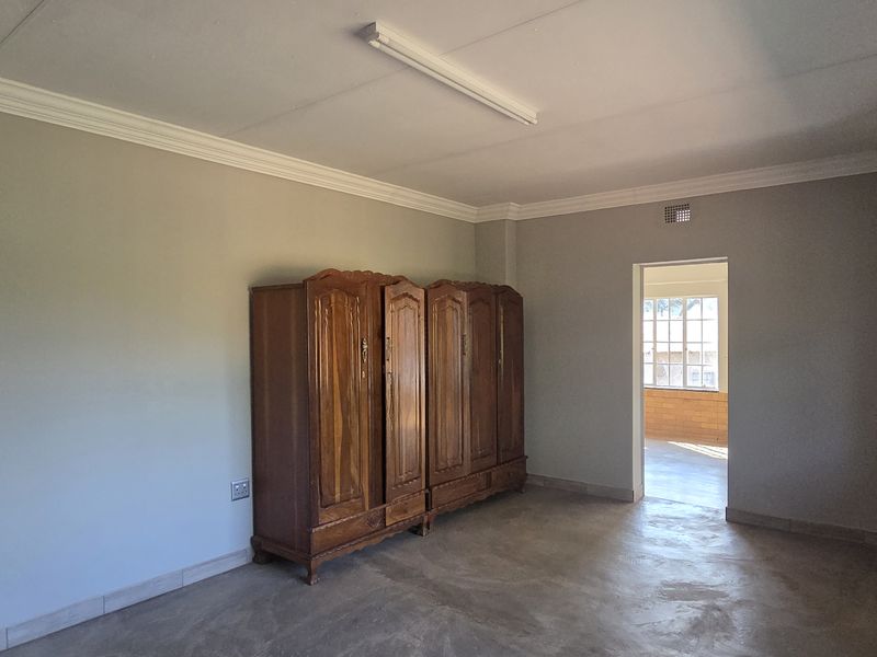 A spacious bedroom featuring neutral walls, cornice detailing, and steel-framed windows, offering a blank canvas for interior design updates.