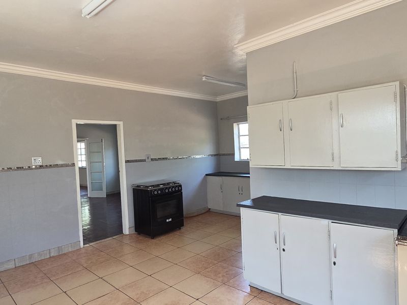 A functional kitchen featuring tiled flooring, built-in cabinetry, a tiled backsplash, and a freestanding stove, offering a practical layout with access to adjacent rooms.