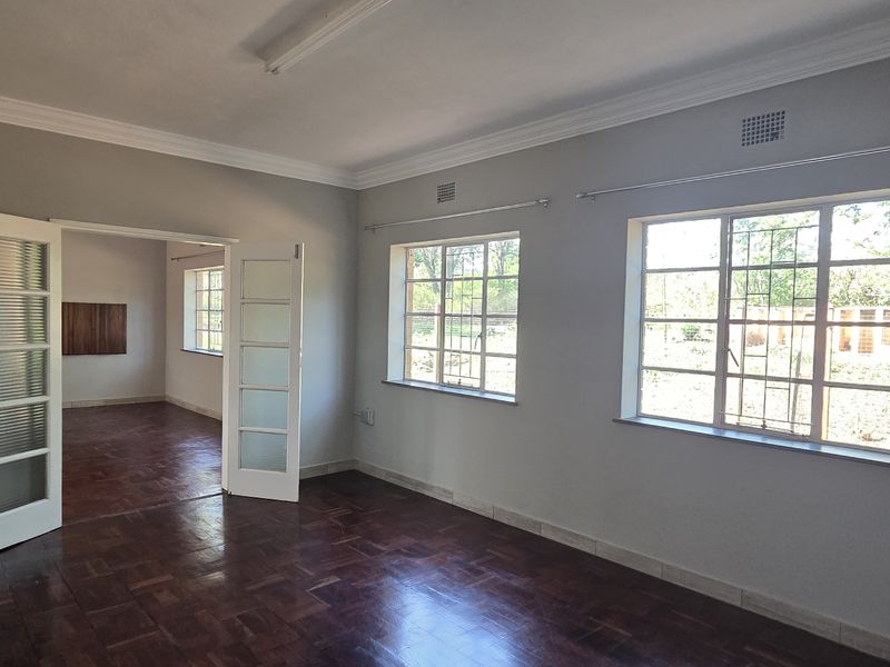 A bright, empty living room featuring classic parquet flooring, crown molding, and large steel-framed windows that provide ample natural light.