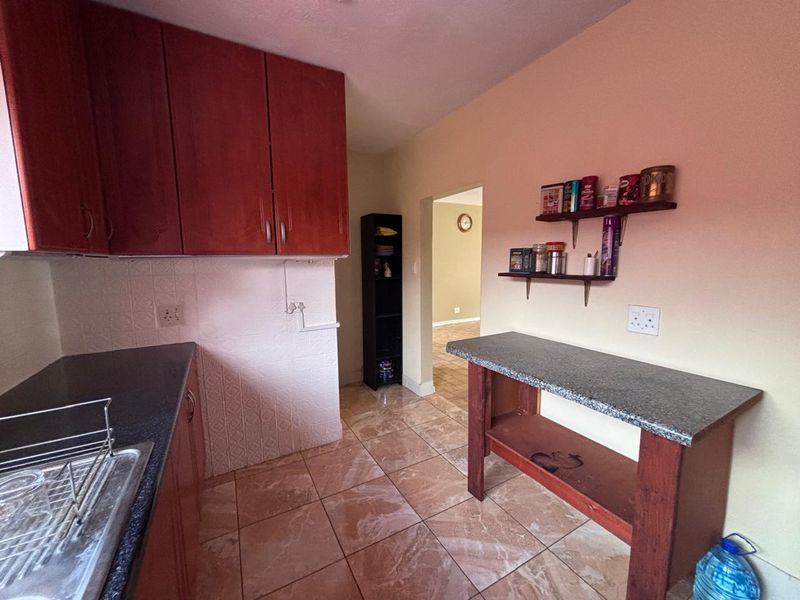 A functional kitchen featuring laminate cabinetry, granite countertops, and tiled flooring, offering a practical layout with potential for modern cosmetic updates.