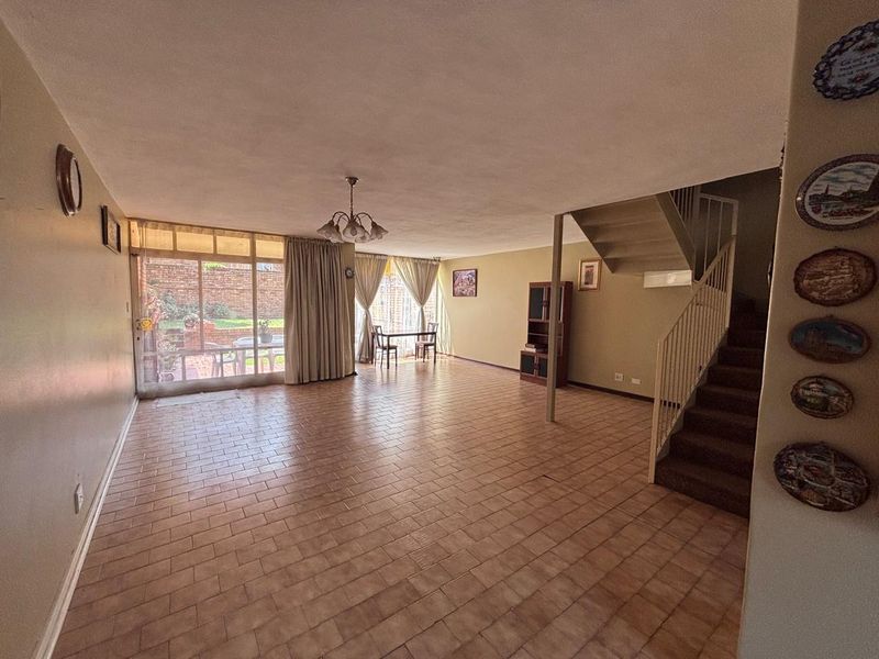Spacious open-plan living area featuring tiled flooring, a staircase, and large sliding glass doors providing access to the rear garden.