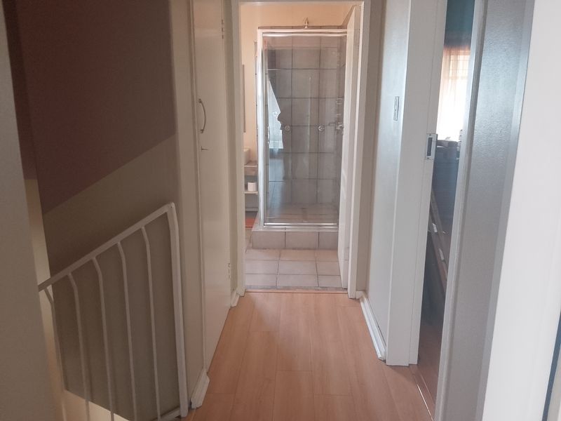 A hallway with laminate flooring leading to a bathroom featuring a tiled shower enclosure and built-in storage.