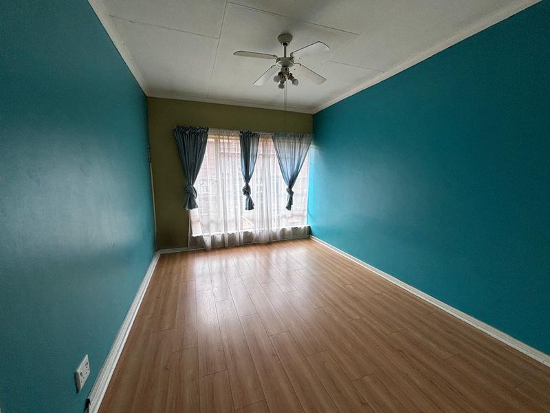 An empty bedroom featuring laminate flooring, a ceiling fan, and blue painted walls, offering a blank canvas for personalization.