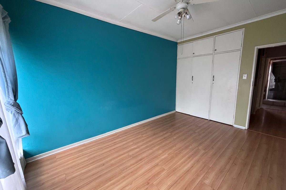A spacious bedroom featuring laminate flooring, built-in cupboards, and a ceiling fan, offering a blank canvas for personalization.