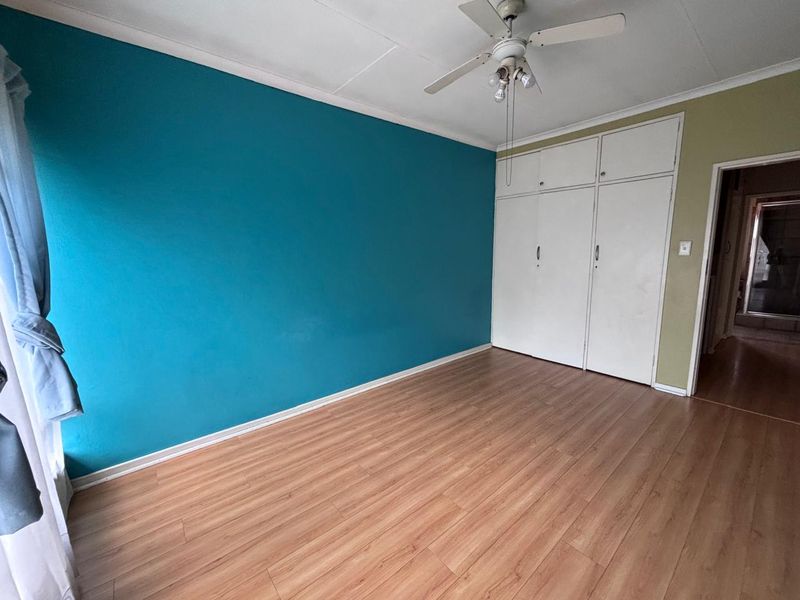 A spacious bedroom featuring laminate flooring, built-in cupboards, and a ceiling fan, offering a blank canvas for personalization.