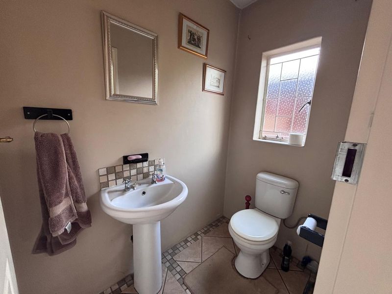 A compact guest bathroom featuring a pedestal basin, toilet, and tiled flooring with a decorative leaded glass window.