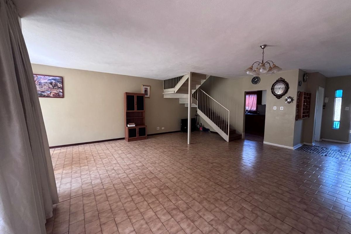 Spacious open-plan living area featuring tiled flooring and a central staircase leading to the upper level.