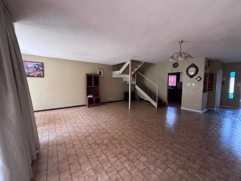 Spacious open-plan living area featuring tiled flooring and a central staircase leading to the upper level.