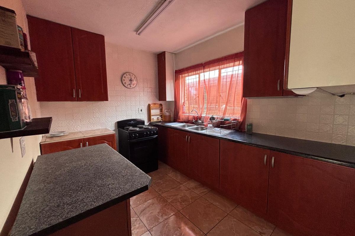 A functional kitchen featuring dark wood-look cabinetry, stone-effect countertops, a double sink, and a freestanding stove with tiled splashbacks and flooring.