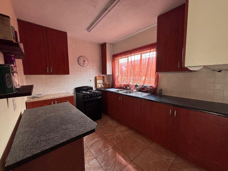 A functional kitchen featuring dark wood-look cabinetry, stone-effect countertops, a double sink, and a freestanding stove with tiled splashbacks and flooring.