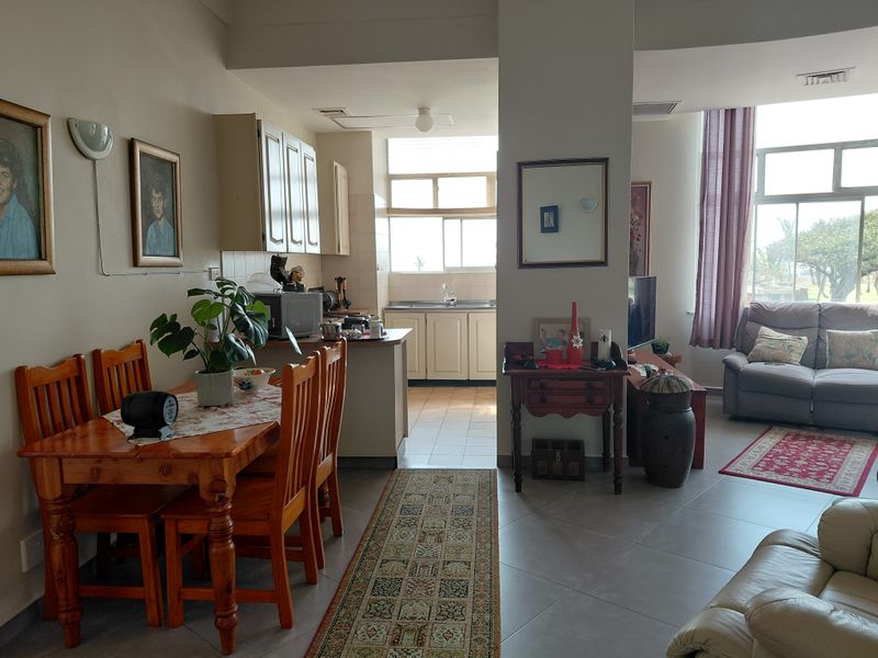Open-plan living and dining area featuring tiled floors, integrated kitchen cabinetry, and large windows providing natural light.