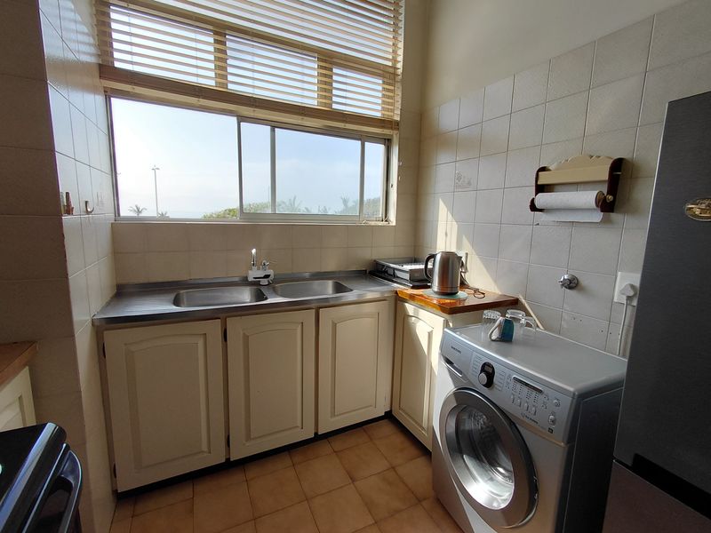 A functional laundry area featuring a stainless steel double sink, tiled splashbacks, built-in cabinetry, and space for a washing machine.