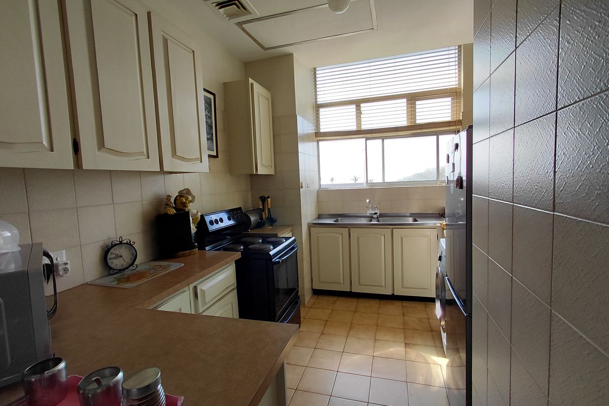 A functional kitchen featuring built-in cabinetry, laminate countertops, a double basin sink, and tiled flooring, offering a practical layout with natural light.