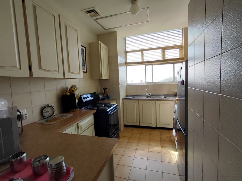 A functional kitchen featuring built-in cabinetry, laminate countertops, a double basin sink, and tiled flooring, offering a practical layout with natural light.