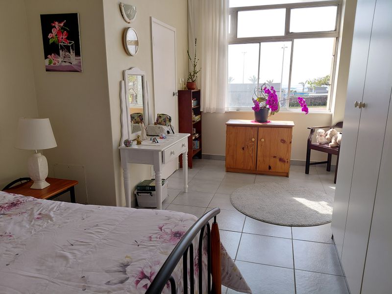 A bright bedroom featuring tiled flooring, a built-in wardrobe, and a large window providing natural light and exterior views.