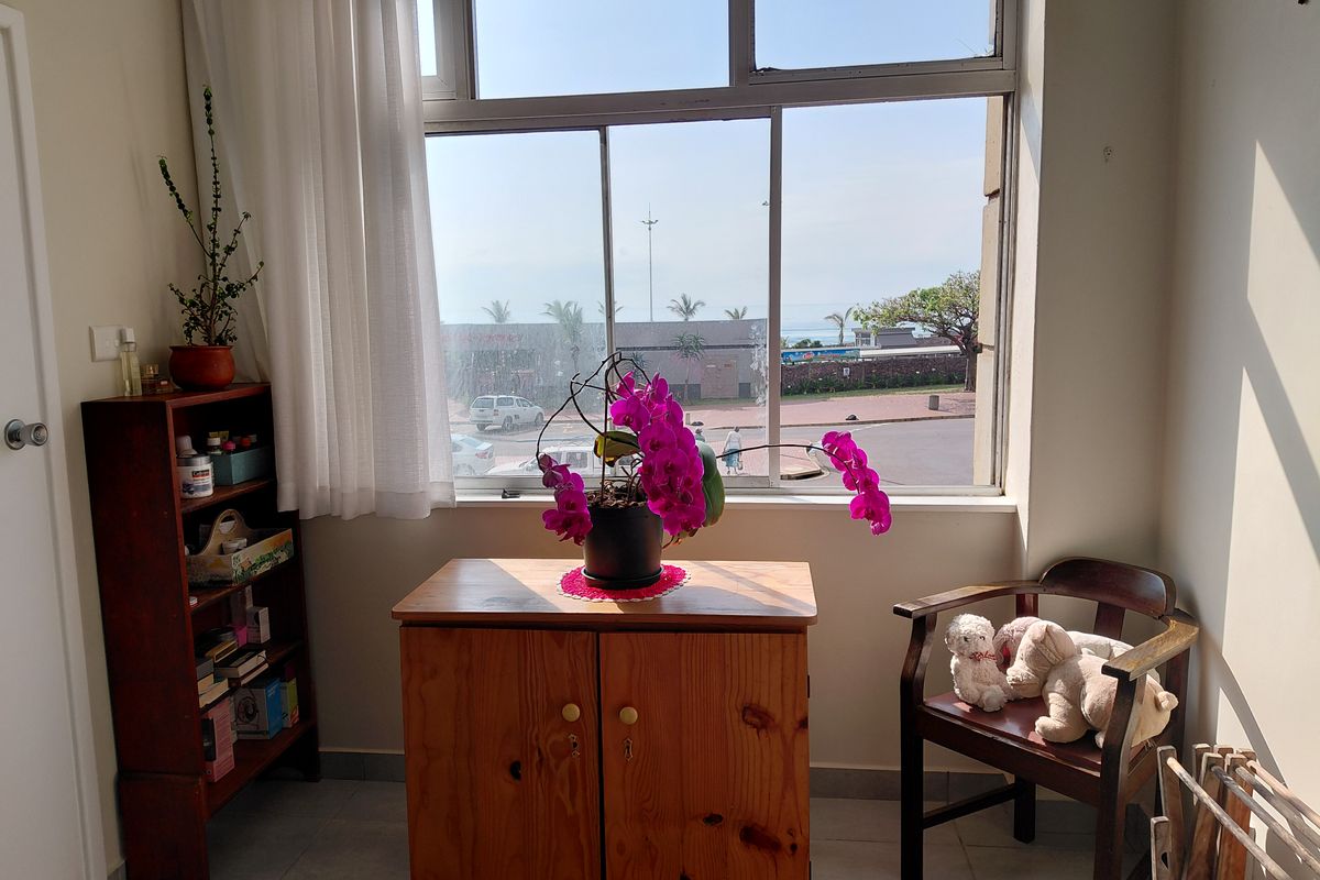 A bright bedroom area featuring large windows with natural light and views, finished with tiled flooring and neutral wall tones.