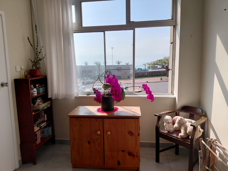 A bright bedroom area featuring large windows with natural light and views, finished with tiled flooring and neutral wall tones.