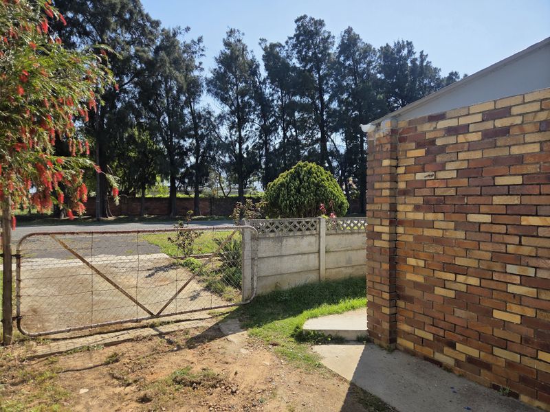 Exterior view of the property featuring a face brick wall, concrete pathway, and a metal driveway gate leading to the front yard area.