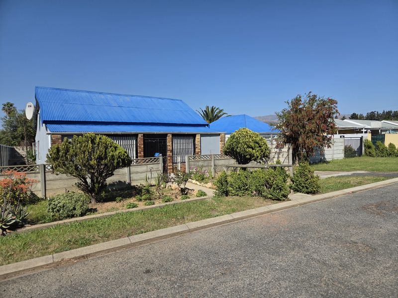 Front view of a residential property featuring a distinctive blue corrugated metal roof, secure boundary wall, and established garden area.