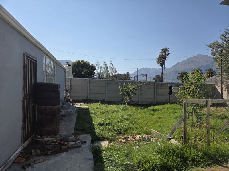 Rear garden area featuring a precast concrete boundary wall, concrete pathway, and mountain views, requiring landscaping and maintenance.
