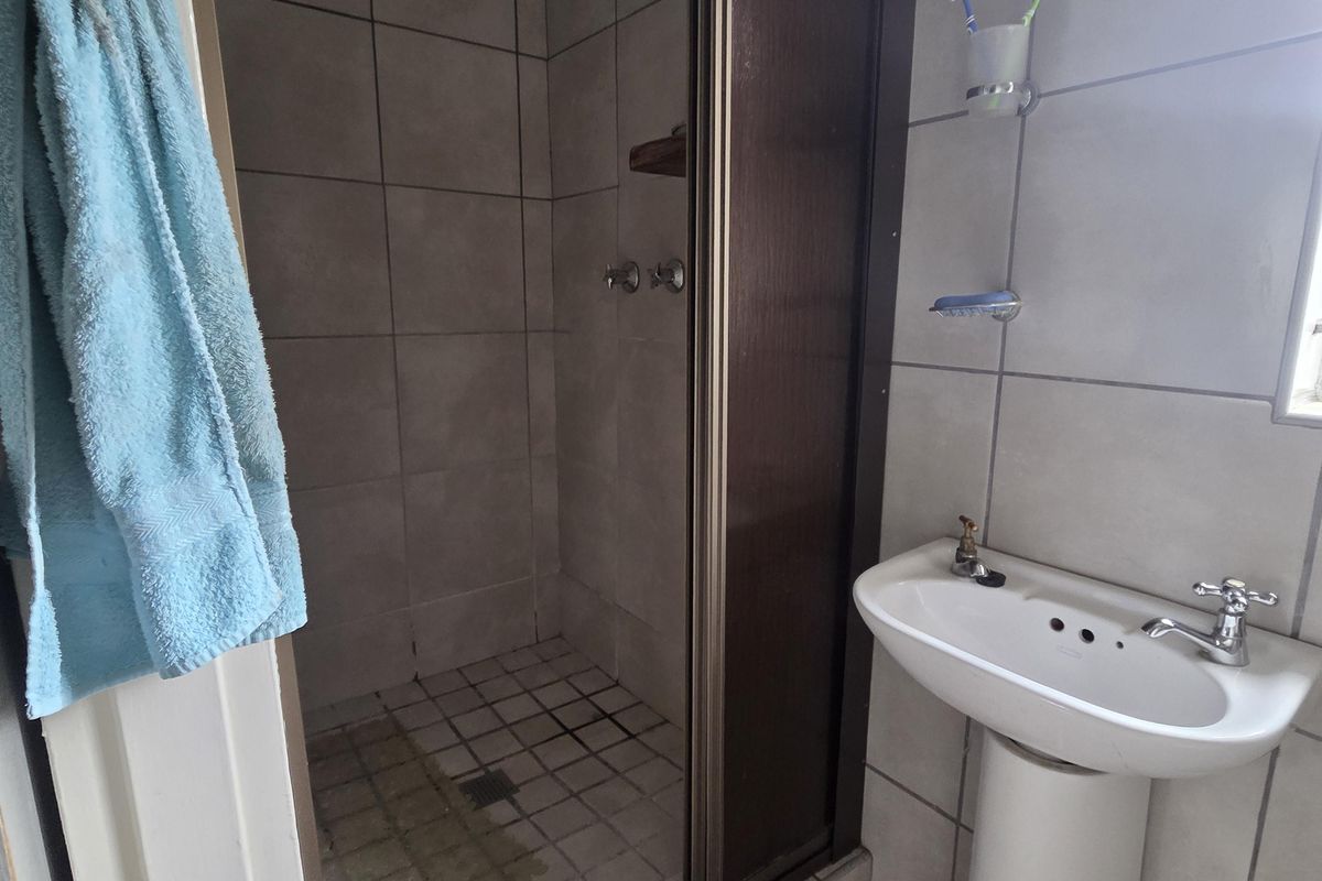 A functional bathroom featuring a pedestal basin and a shower enclosure with tiled finishes, requiring some maintenance and cosmetic updates.